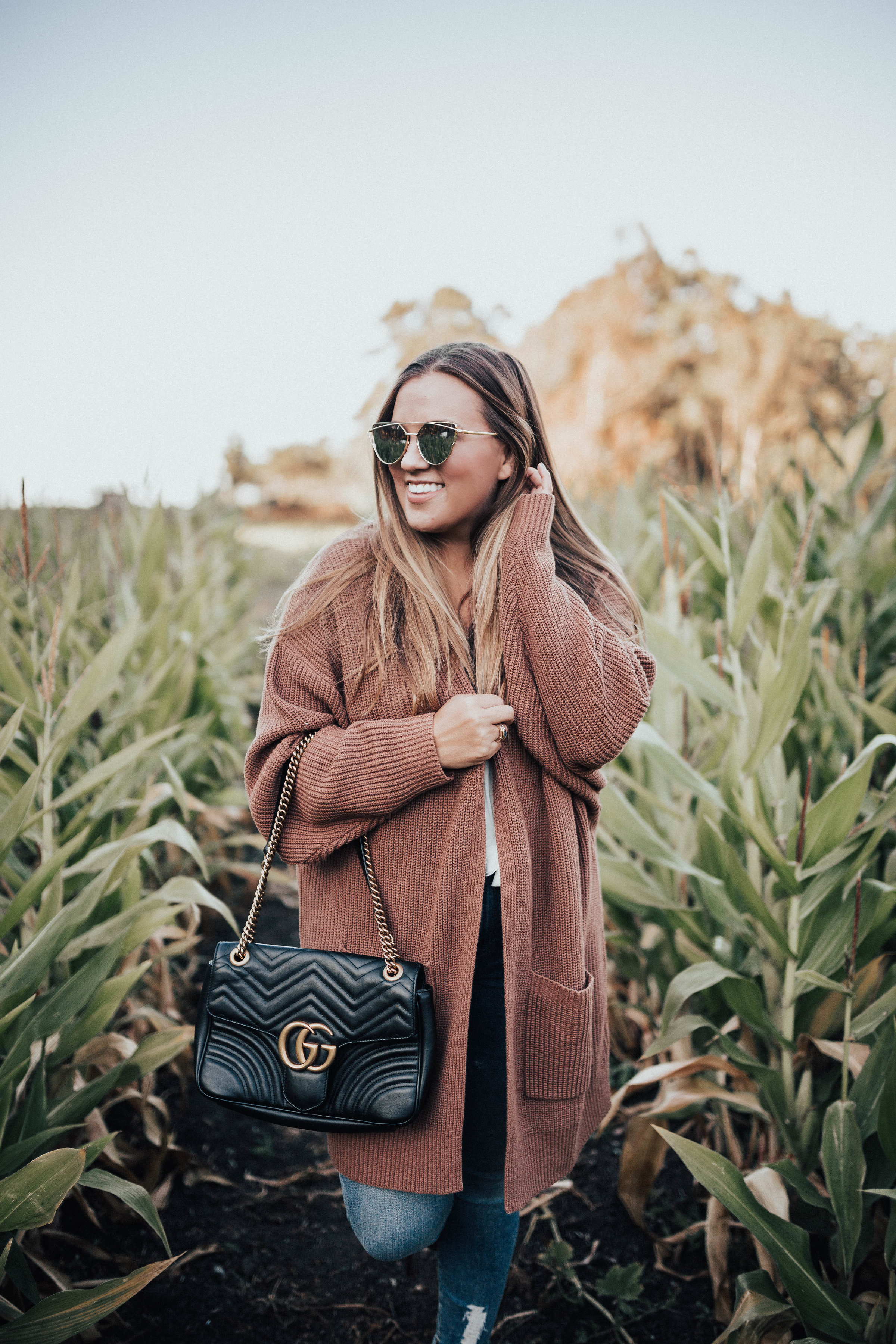 Ashley Zeal from Two Peas in a Prada shares her fall uniform. She is wearing an oversized cardigan, Good American Jeans, booties and a Gucci bag. 