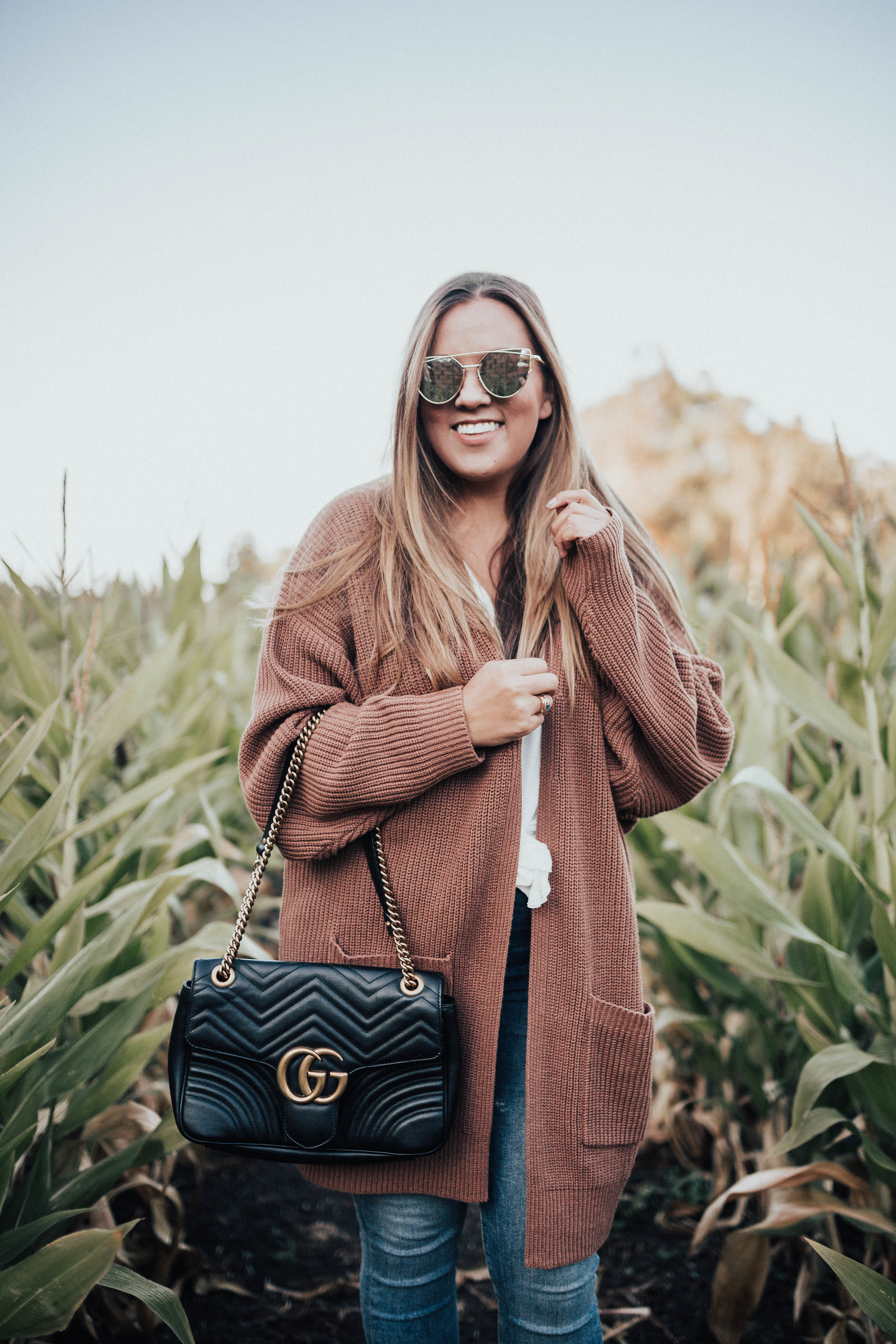 Ashley Zeal from Two Peas in a Prada shares her fall uniform. She is wearing an oversized cardigan, Good American Jeans, booties and a Gucci bag. 