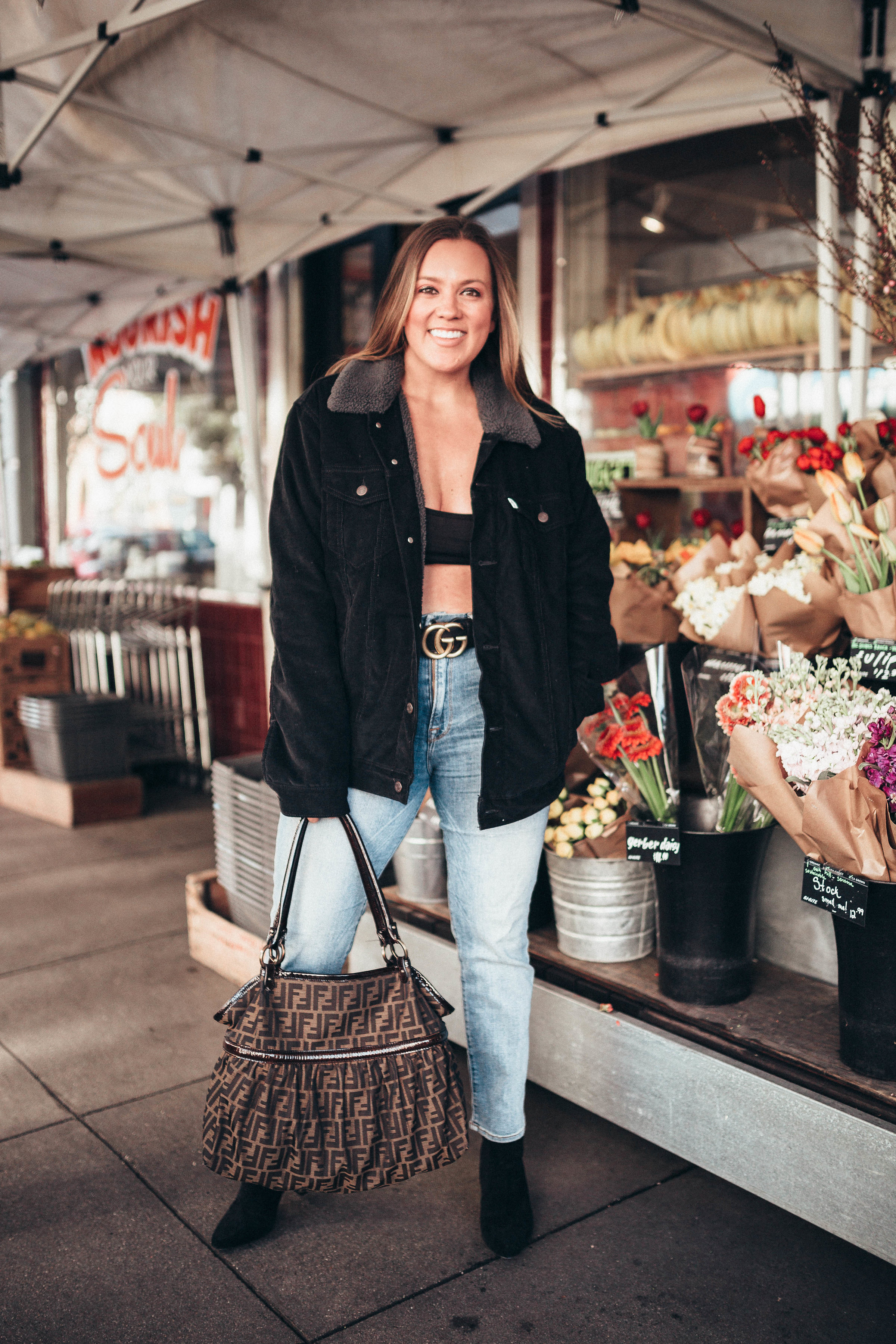 Ashley Zeal from Two Peas in a Prada shares an outfit using her boyfriend's jacket. She is wearing a Levi's jacket, Good American Jeans and a GG Gucci belt. 