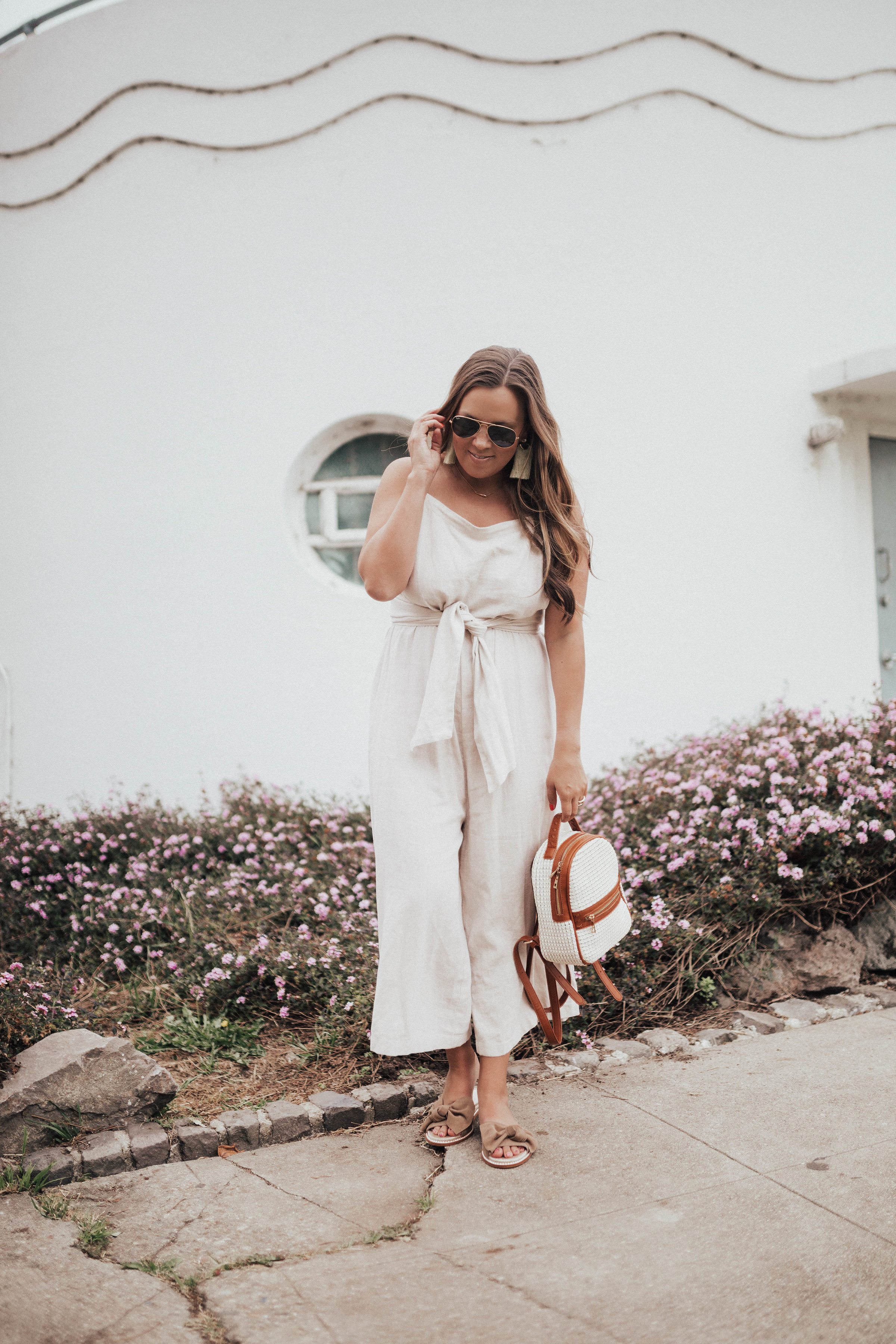 Ashley Zeal from Two Peas in a Prada wears a beige BP linen jumpsuit from Nordstrom that is under $60. She is wearing Caslon sandals and Sole Society bag. 