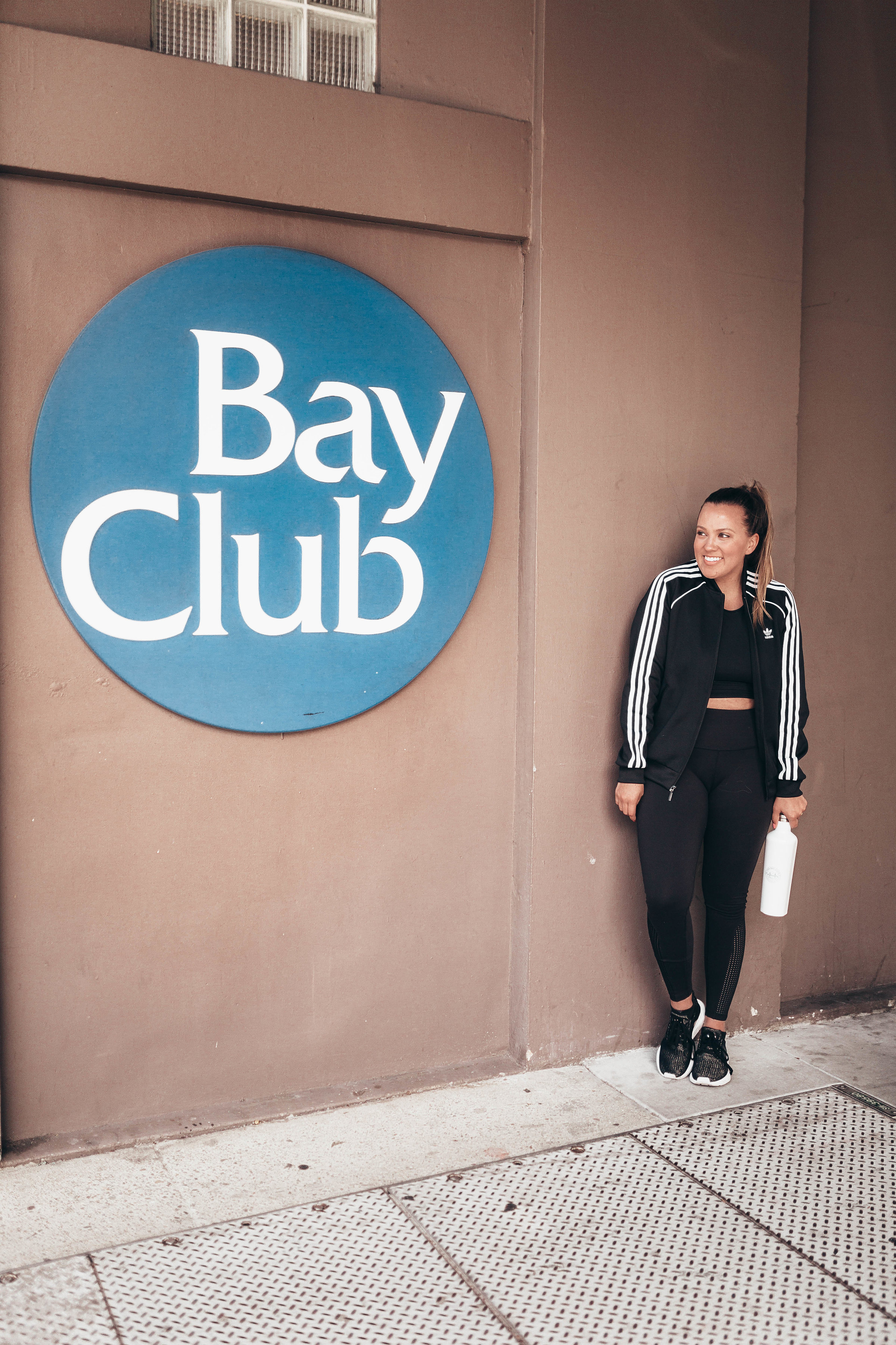 Ashley Zeal from Two Peas in a Prada shares a six month review of Bay Club San Francisco. She is wearing Splits 59 leggings and an Adidas jacket and sneakers. 